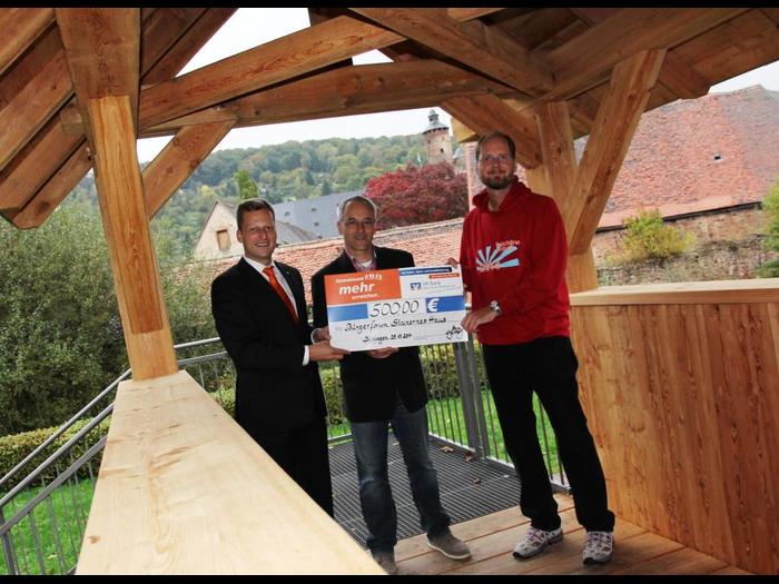 Mario Gerhardt (VR Bank) übergibt den symbolischen Spendenscheck an Dr. Hubertus Protz und Hans-Joachim Beckmann